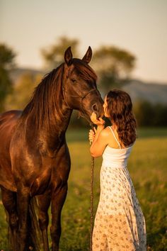 a woman in a dress standing next to a brown horse