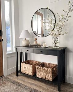 a black console table with baskets under a round mirror