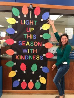 a woman standing in front of a sign that says light up this season with kindness