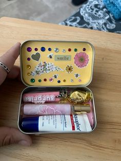 a person is holding a small tin with various items in it on a wooden table