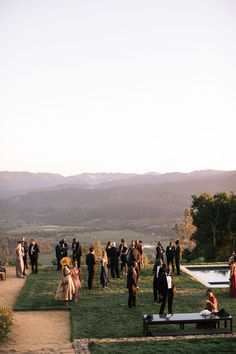 a group of people standing on top of a lush green field next to a lake