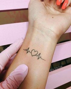 a woman's arm with a heart and heartbeat tattoo on her left wrist, next to a pink manicure