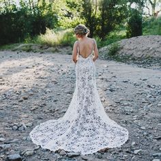 a woman in a white wedding dress standing on the ground looking at trees and rocks