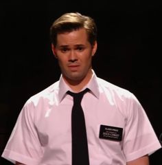 a man in a white shirt and black tie with a name tag on his chest