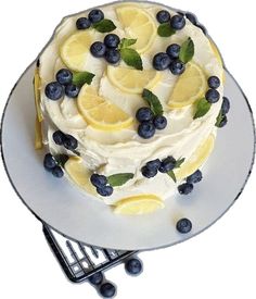 a cake with lemons, blueberries and mint leaves on top is sitting on a plate