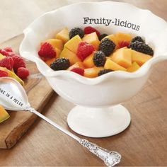 a white bowl filled with fruit on top of a wooden cutting board next to a spoon