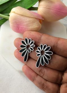 a pair of black and white flower shaped earrings on a person's hand with tulips in the background