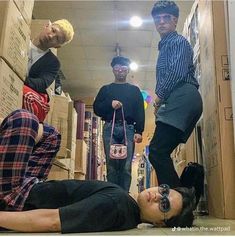 three young men standing and laying on the floor in a room with cardboard boxes all around them