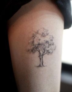 a woman's arm with a small tree tattoo on the back of her shoulder