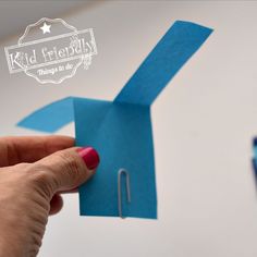 a hand holding a piece of blue paper next to a pair of scissors on a white surface