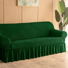 a green couch sitting on top of a wooden floor next to a potted plant