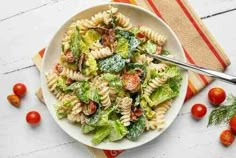 a white bowl filled with pasta salad next to cherry tomatoes and green lettuce