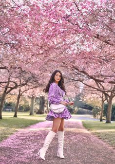 a woman in purple dress and white boots standing under pink blossom trees