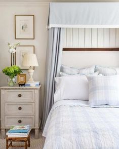 a bed with white sheets and pillows in a bedroom next to a nightstand with flowers on it