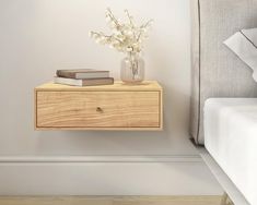 a nightstand with flowers and books on it next to a bed in a white room