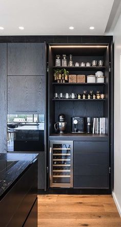 a kitchen with black cabinetry and wooden flooring in the center is lit by recessed lights