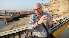 a man with glasses standing in front of a body of water and lots of boats