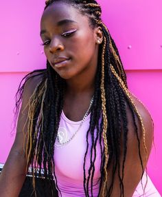 a woman with dreadlocks sitting in front of a pink wall