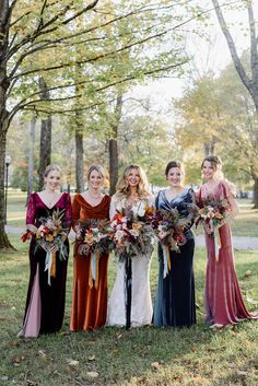 a group of women standing next to each other holding bouquets in front of trees