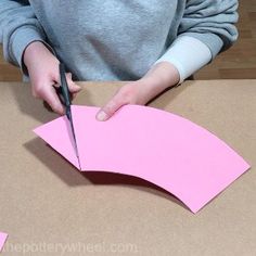 a person cutting out pink paper with scissors