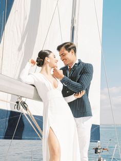 a man standing next to a woman on top of a sail boat in the ocean