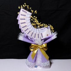 the money is wrapped in purple ribbon and gold bow with flowers on top, sitting on a white table