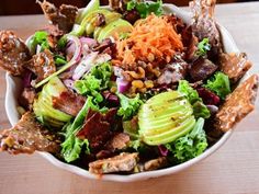 a white bowl filled with lots of food on top of a wooden table