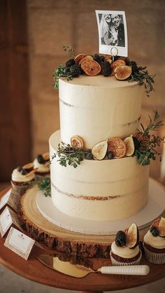 a three tiered wedding cake on a table with cupcakes and an old photo