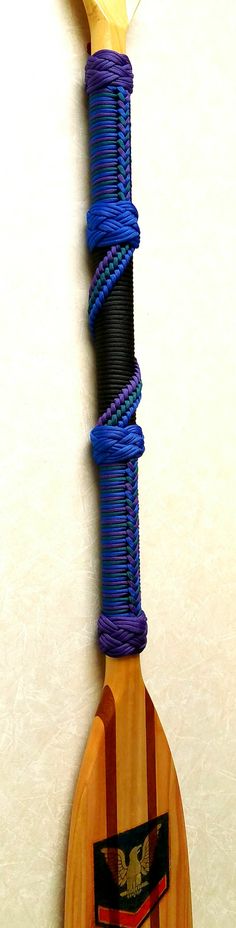 a wooden paddle with blue and purple cords attached to it's end, against a white wall