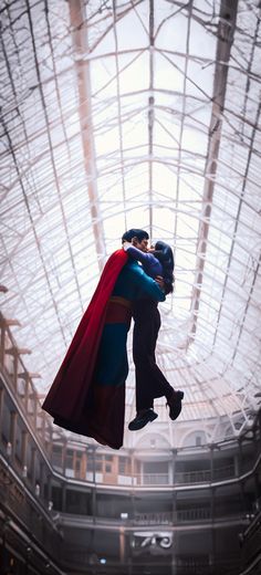 two people in superman costumes are hugging under a glass ceiling