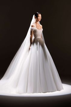 a woman in a white wedding dress with a veil on her head, standing against a dark background