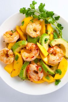 a white bowl filled with shrimp, peppers and avocado on top of a table