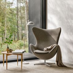 an egg chair with a blanket draped over it in front of a window and table