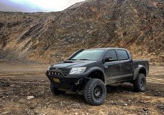 a black pick up truck parked on top of a dirt covered field next to a mountain