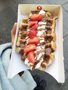 a person holding up a waffle with strawberries and chocolate sauce on the top