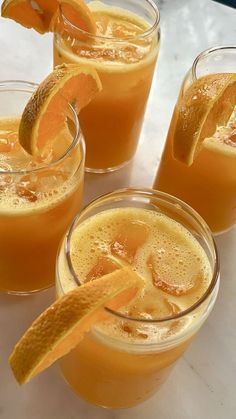 three glasses filled with orange juice and garnished with an orange peel on the rim