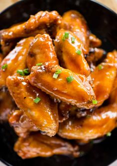 a black bowl filled with chicken wings covered in sauce and garnished with parsley