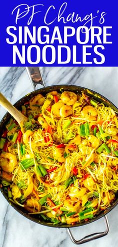 a pan filled with noodles and vegetables on top of a marble counter next to a blue sign