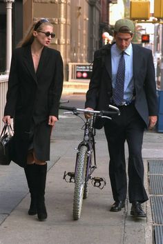 a man and woman walking down the street with a bicycle