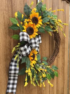 a wreath with sunflowers and greenery hanging on a wooden door, decorated with gingham ribbon