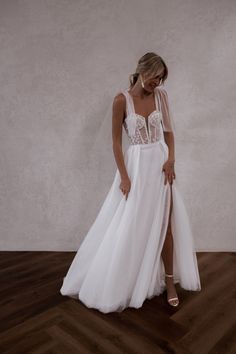 a woman in a white wedding dress standing on a wooden floor with her legs crossed