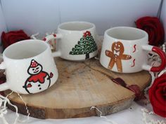 three coffee mugs with christmas designs on them sitting on a piece of wood next to red roses