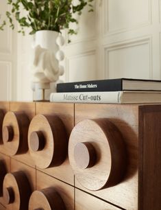 a book on top of a wooden dresser with books and vase in the back ground