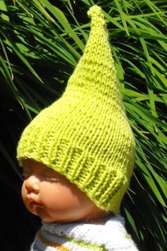 a baby doll wearing a green knitted hat and scarf in front of some grass