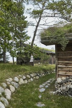 an old log cabin with grass on the roof and stone pathway leading up to it