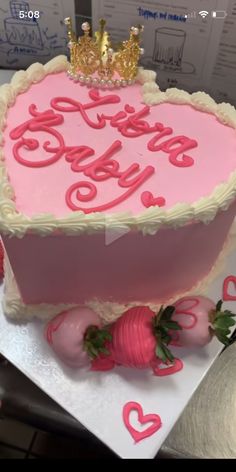 a pink heart shaped cake with strawberries on the bottom and two gold crowns on top