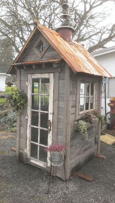 a small wooden shed sitting in the middle of a gravel lot next to a house