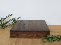 a wooden box sitting on top of a table next to green leaves and a plant