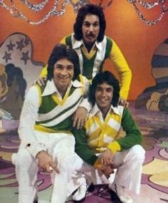 three men in green and yellow outfits posing for a photo on the set of tv show