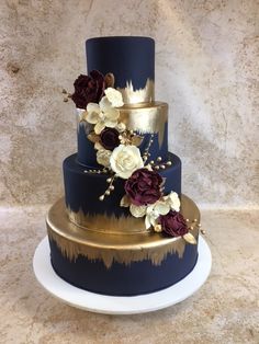 a three tiered blue and gold wedding cake with flowers on the top, sitting on a white plate